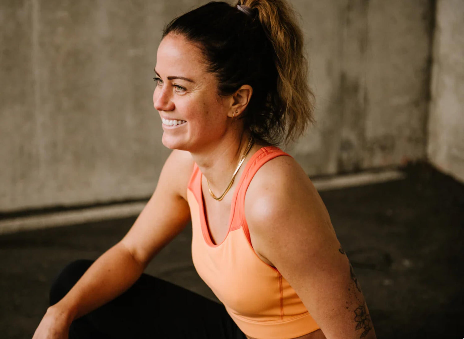 a woman in an orange sports bra sitting down and smiling.