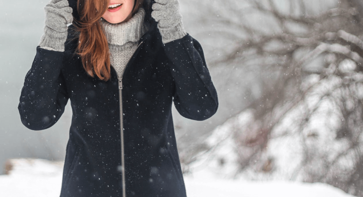 a woman wearing a winter hat and gloves with snow falling around her