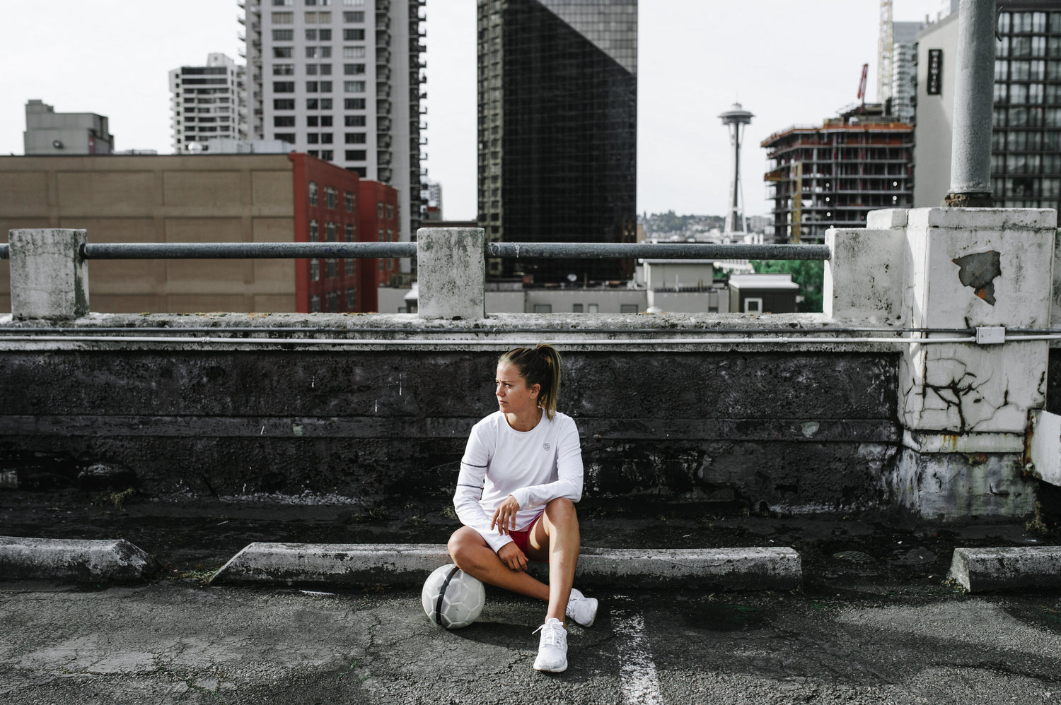 a woman sitting on top of an urban rooftop with a soccer ball resting under her knee