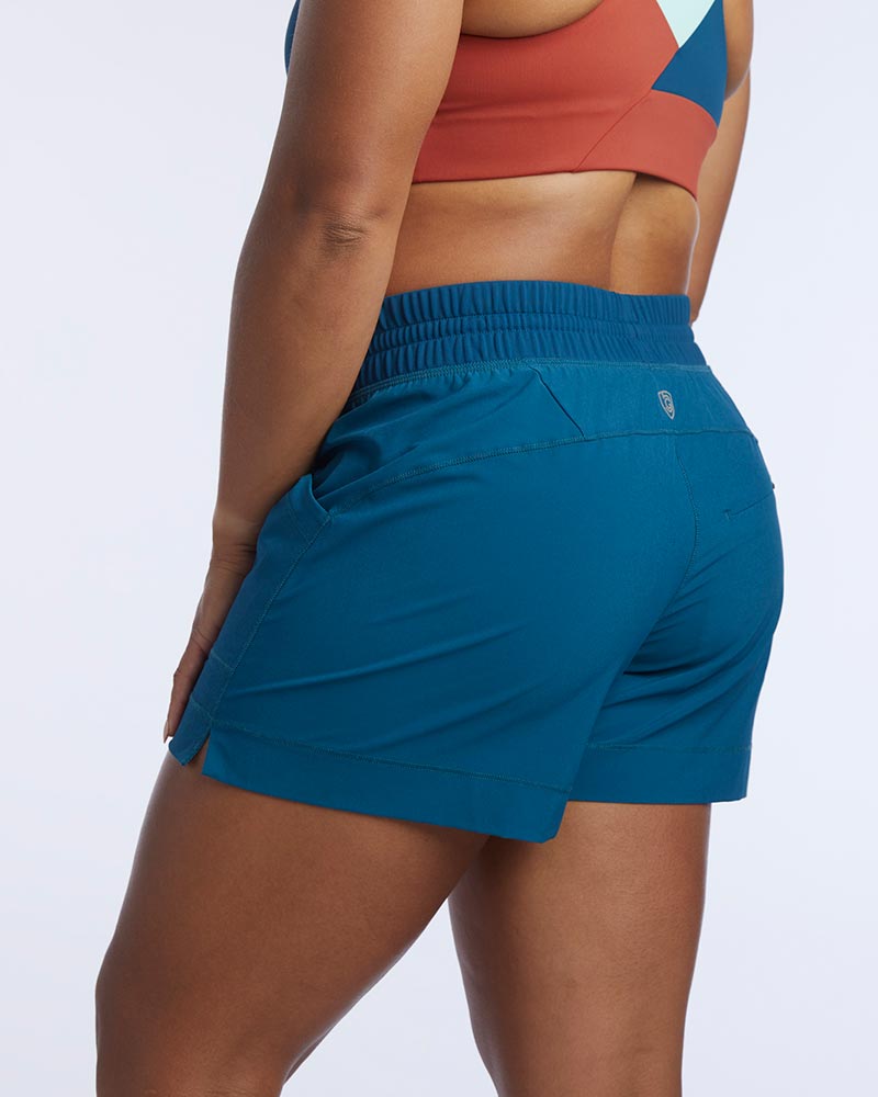 A woman poses in Triple V women's athletic shorts with pockets in teal.