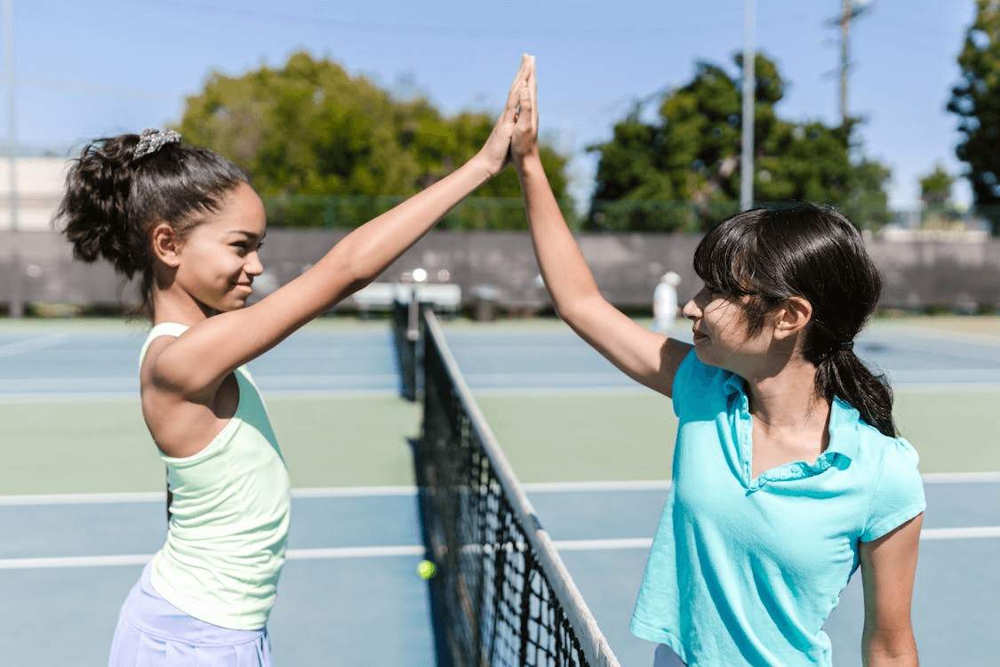 2 young girl tennis players high-fiving each other by the net
