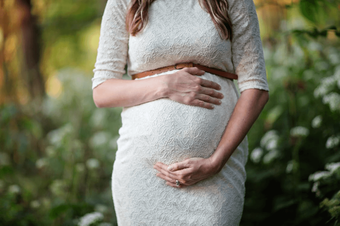 a pregnant woman in a white dress with her arms crossed around her enlarged belly area