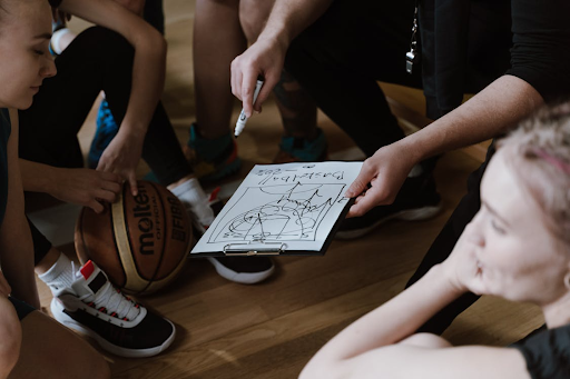 A group surrounding a coach who is holding a playbook