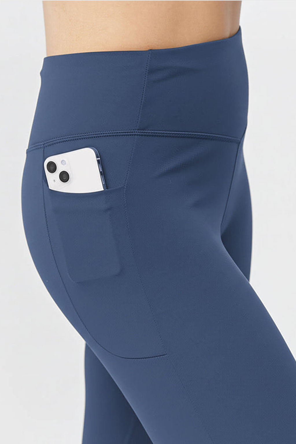 A person wearing Go Again Women's Cropped Leggings, length 21", in blue with a high-rise waistband and a white smartphone in the side pocket, stands against a plain light background.