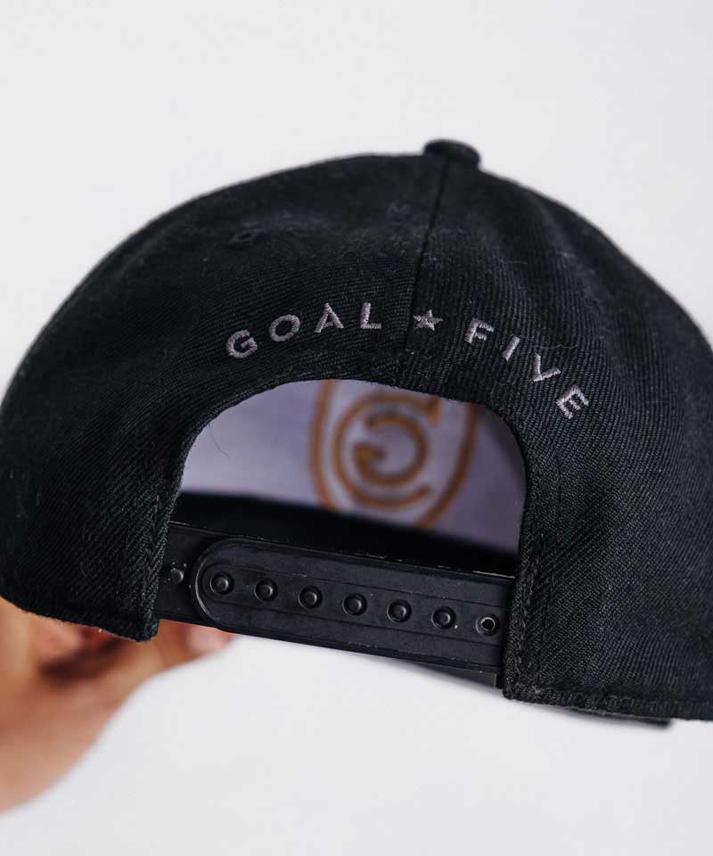 The Goal Five branding and snap back of the black flat brim hat are featured.