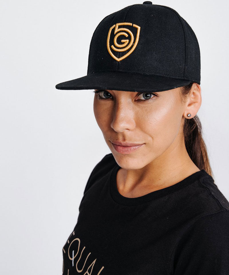 The model displays the raised gold embroidered G5 logo on the flat brim snap back hat.