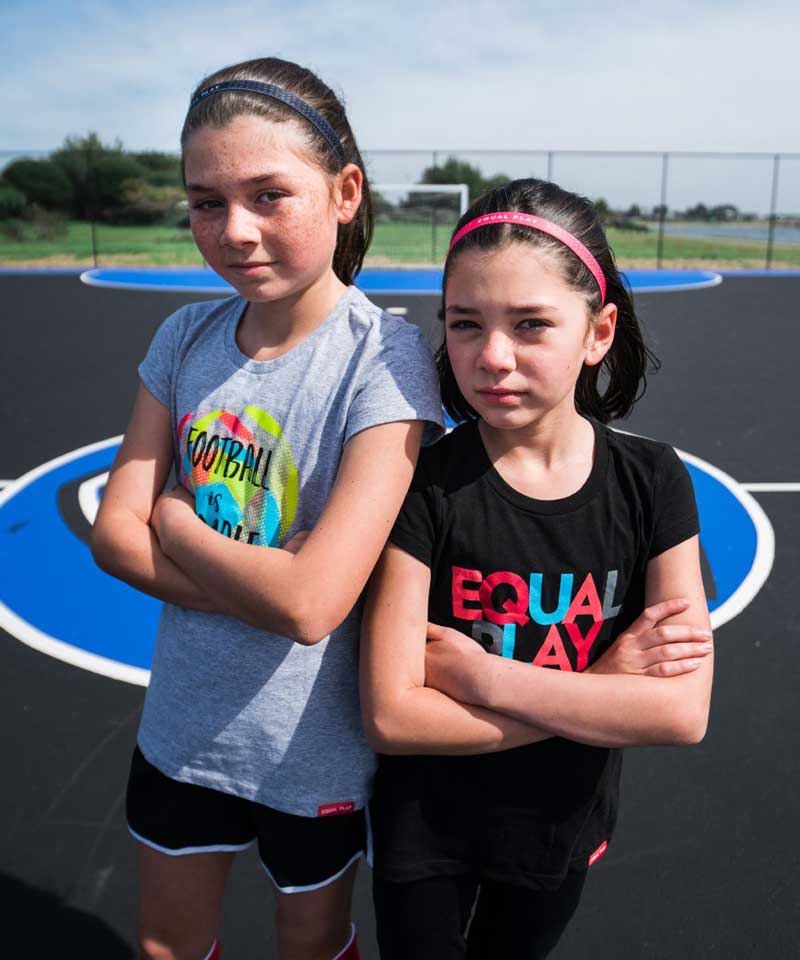 A tween girl wears the Equal Play girls' black T shirt training outside with a friend.