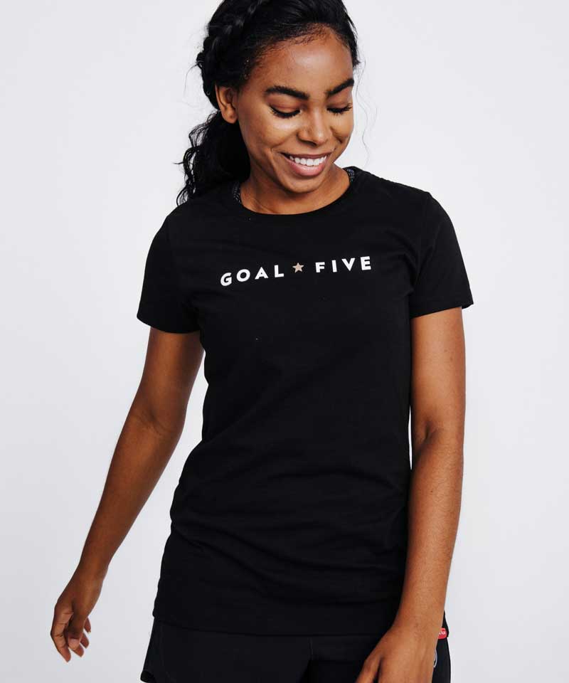 A woman smiles wearing a Goal Five women's athletic t-shirt.